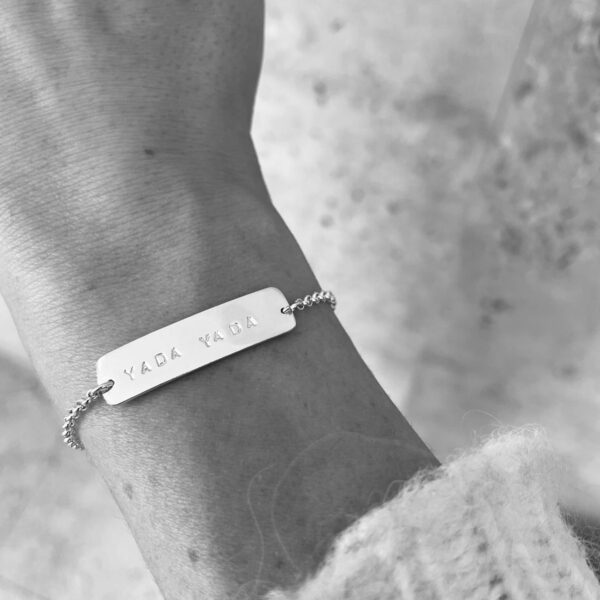 A wrist wearing a silver bracelet with the words "Yada Yada"