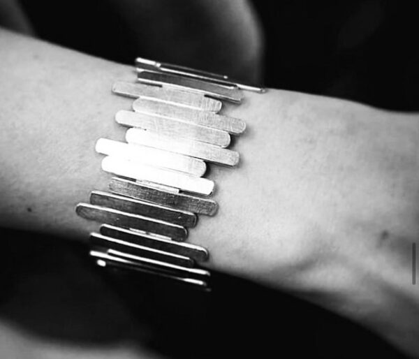 A wrist wearing a handmade silver bracelet shaped as sticks put together randomly