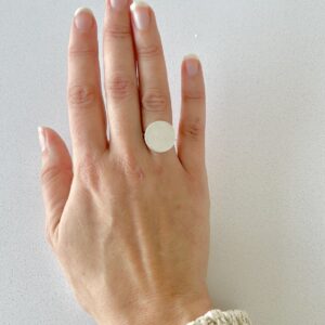 A hand wearing a matte handmade silverring shaped as a coin.