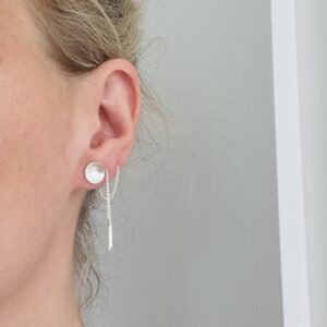 An ear wearings one small bowl shaped silverearring and one silver earchain.