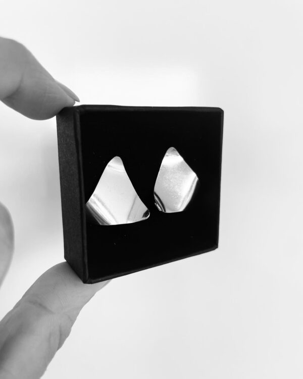 Two fingers holding a black jewelry box showing two silver earrings shaped as wavy triangles,