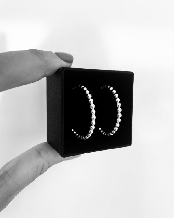 Two fingers holding a black jewelry box with a pair of silver hoops