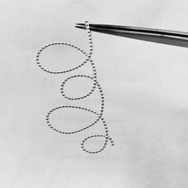 A tweezer holding one silver earring shaped as four loops of dotted silver wire