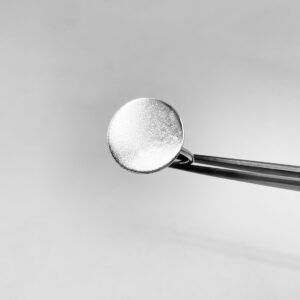 A tweezer holding a silver ring shaped as a matte coin