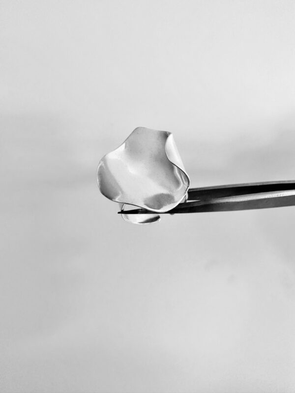 A tweezer holding a handmade silver ring shaped as a rose petal