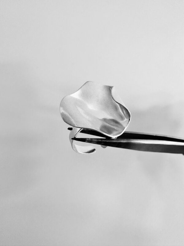 A tweezer holding a handmade silver ring shaped as a rose petal