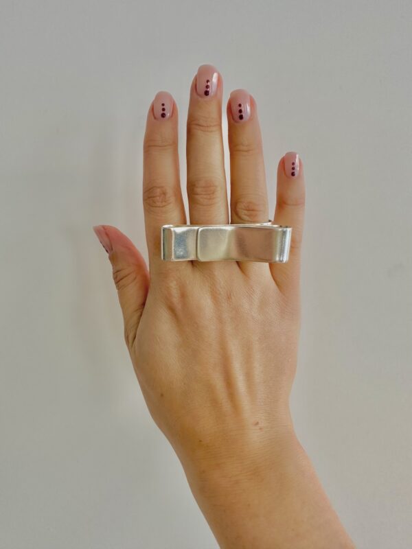 A hand wearing a handmade silver ring shaped as a big swirl.