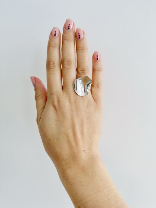 A hand wearing a shiny silver ring shaped as a rose petal.