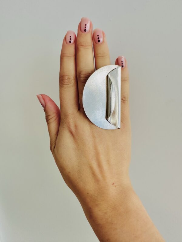 A hand wearing a handmade silver ring shaped as a big coin with on side folded.