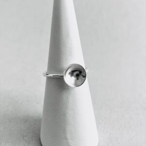 A white ring holder with a thin silver ring with a small silver bowl.