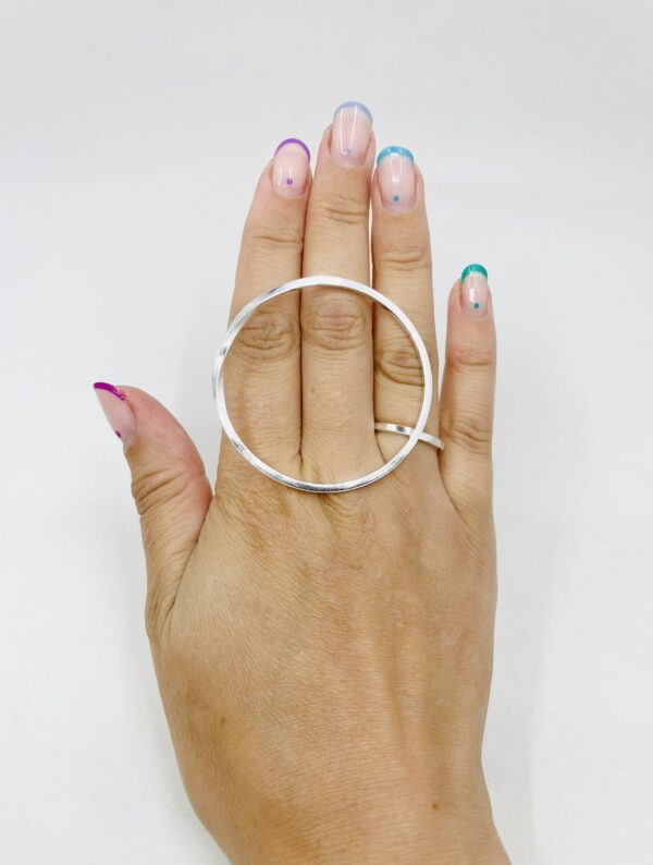 A hand with rainbow coloured nail polished wearing a big silver ring shaped as a twisted circle