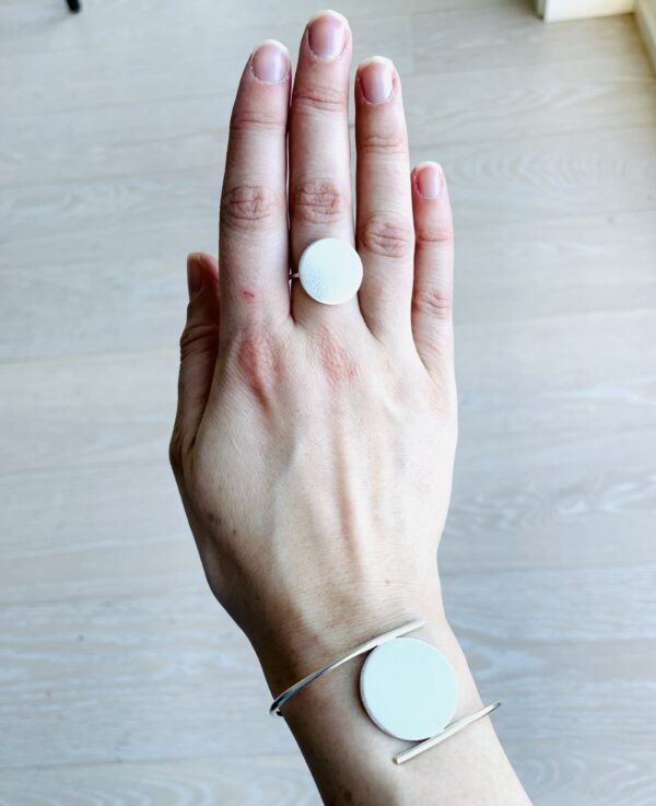 A hand and wrist wearing a silver ring and bracelet shaped as as matte coins