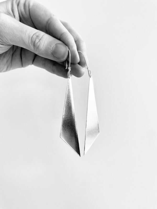 A hand holding a pair of hanging silver earrings shaped as triangles