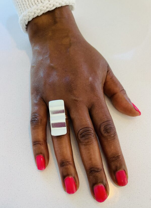 A hand with pink nail polish wearing a silver ring shaped as a wavy recctangle