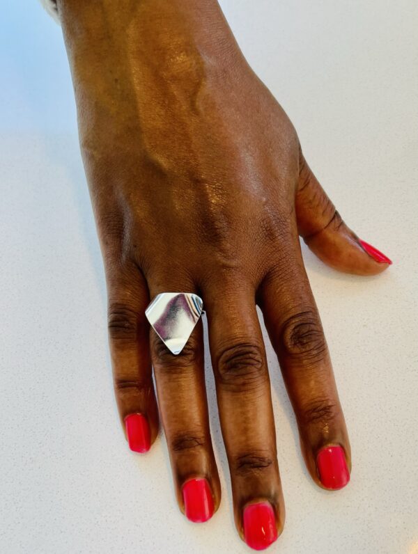 A hand with pink nail polish wearing a silver ring shaped as a wavy traingle