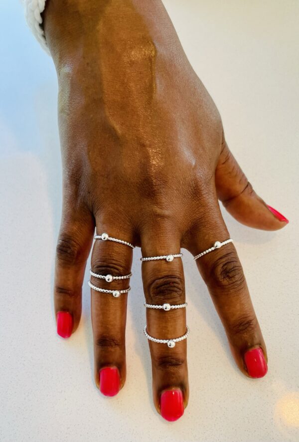 A hand with pink nail polish wearing7 thin silverrings with small dots